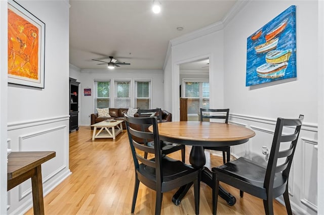 dining area with ornamental molding, ceiling fan, light wood-style floors, a decorative wall, and a wainscoted wall