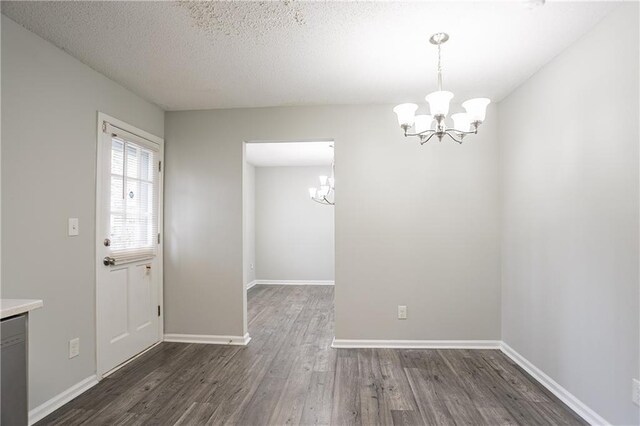 unfurnished dining area featuring a textured ceiling, baseboards, a chandelier, and dark wood finished floors