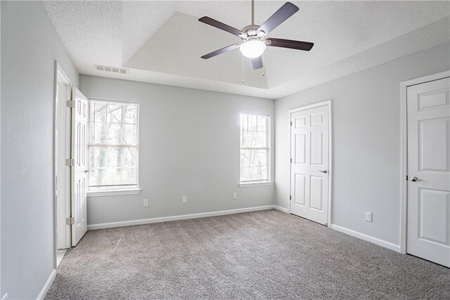 unfurnished bedroom featuring visible vents, multiple windows, carpet, and a raised ceiling