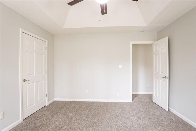 unfurnished bedroom featuring a ceiling fan, a raised ceiling, carpet floors, and baseboards