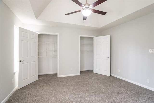 unfurnished bedroom with baseboards, multiple closets, carpet, and a raised ceiling