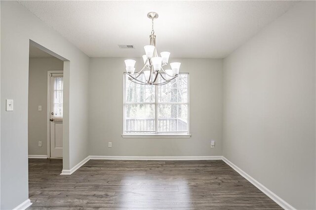 unfurnished dining area featuring an inviting chandelier, wood finished floors, baseboards, and visible vents
