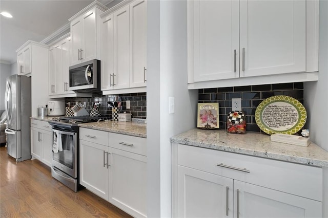 kitchen featuring appliances with stainless steel finishes, light stone counters, tasteful backsplash, wood-type flooring, and white cabinets