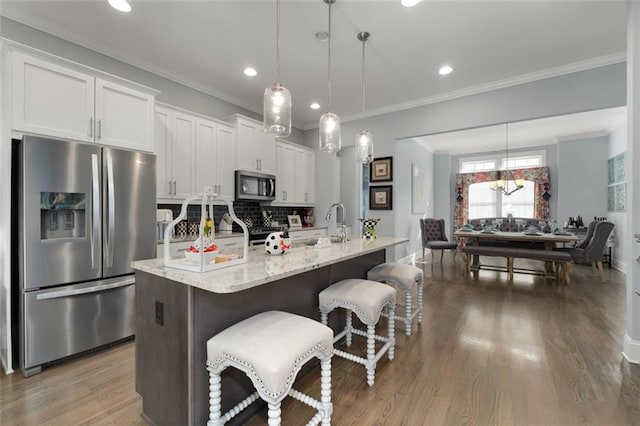 kitchen featuring hanging light fixtures, a kitchen breakfast bar, stainless steel appliances, a kitchen island with sink, and white cabinets