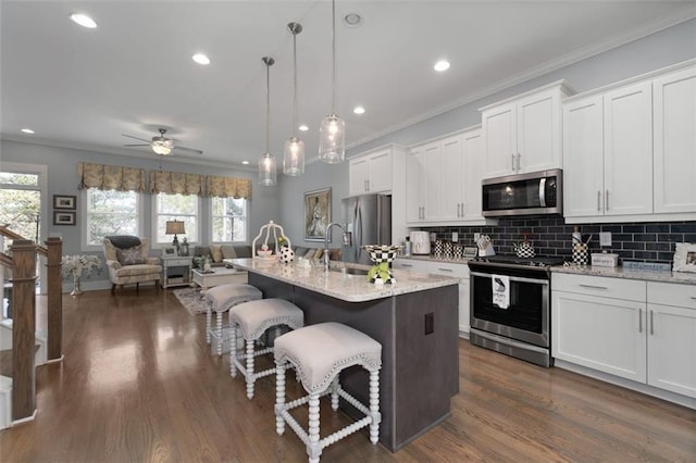 kitchen with stainless steel appliances, a center island with sink, white cabinets, and decorative light fixtures