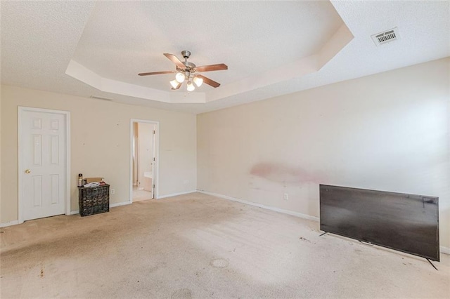 unfurnished bedroom with a tray ceiling, connected bathroom, ceiling fan, and light carpet