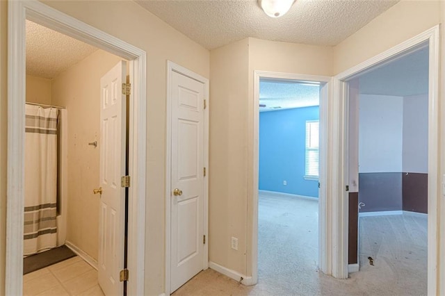 hallway featuring light colored carpet and a textured ceiling