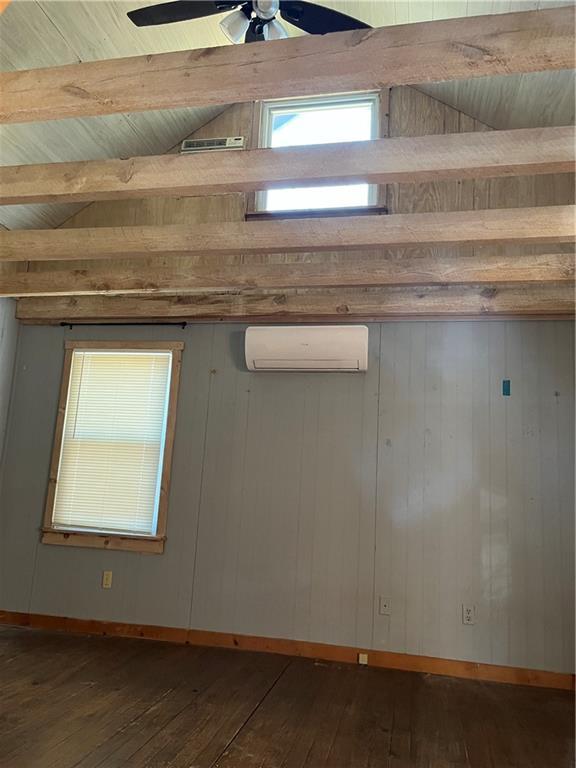 empty room with ceiling fan, dark hardwood / wood-style flooring, a wall mounted AC, and lofted ceiling with beams