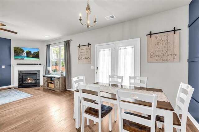 509 Azalea Bloom Dr, Loganville, GA 30052 - dining room featuring a barn door, a glass covered fireplace, ceiling fan with notable chandelier, baseboards, and light wood-type flooring