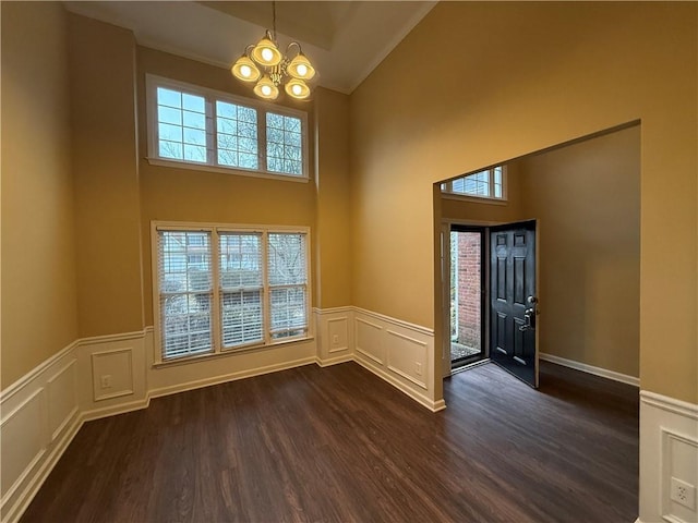 foyer entrance featuring an inviting chandelier, plenty of natural light, dark wood-style flooring, and a wainscoted wall