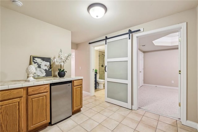 kitchen featuring refrigerator, a barn door, baseboards, light tile patterned floors, and tile countertops