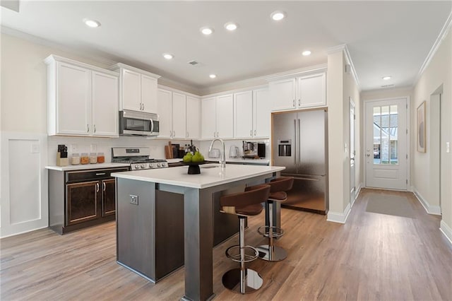 kitchen with white cabinets, a kitchen breakfast bar, light countertops, ornamental molding, and appliances with stainless steel finishes