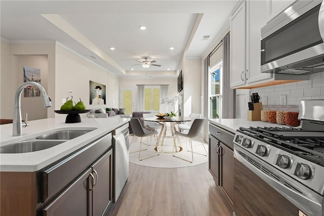 kitchen with stainless steel appliances, a sink, light countertops, a tray ceiling, and light wood finished floors