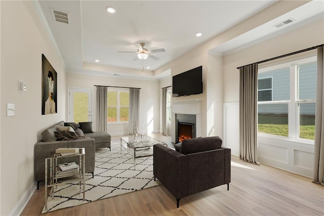 living area with a tray ceiling, a lit fireplace, visible vents, and light wood-style flooring