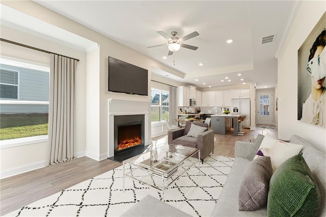 living room with recessed lighting, visible vents, baseboards, light wood-style floors, and a lit fireplace