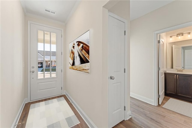 entryway with light wood finished floors, baseboards, visible vents, crown molding, and a sink