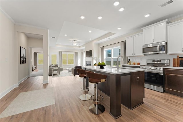 kitchen featuring a kitchen island with sink, stainless steel appliances, a sink, visible vents, and white cabinets