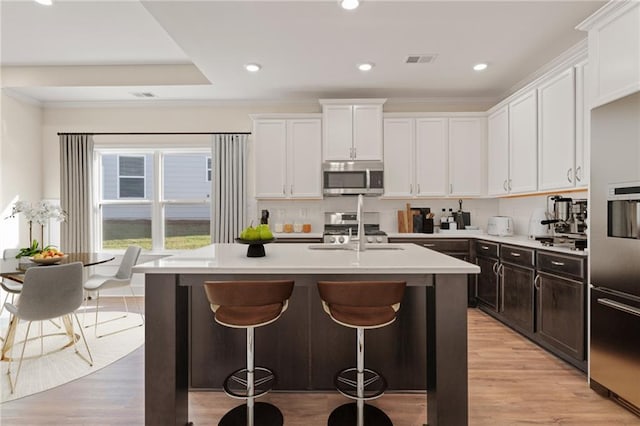 kitchen featuring white cabinets, a breakfast bar area, stainless steel appliances, light countertops, and a sink