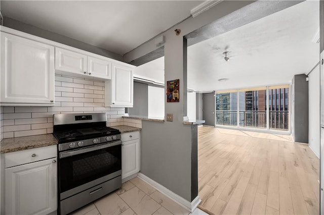 kitchen featuring light stone counters, backsplash, white cabinetry, and stainless steel gas range