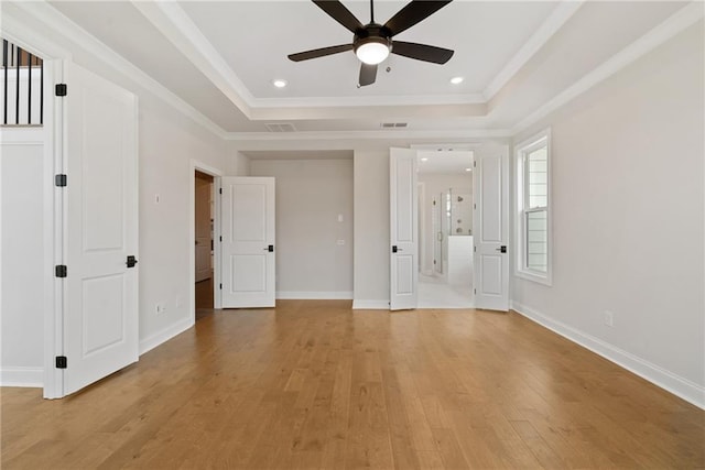 interior space featuring a raised ceiling, ensuite bath, ceiling fan, ornamental molding, and light hardwood / wood-style floors