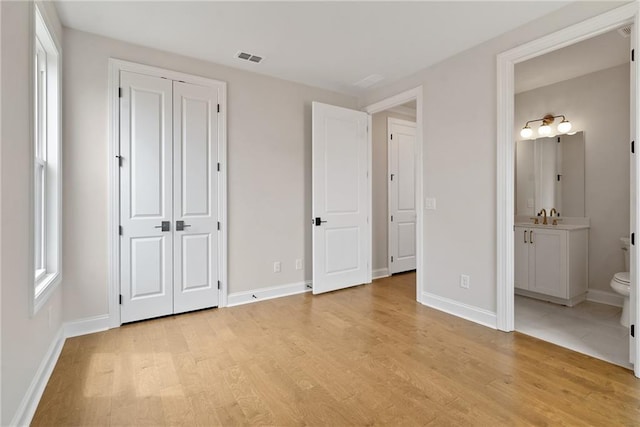 unfurnished bedroom featuring ensuite bathroom, light hardwood / wood-style flooring, a closet, and sink