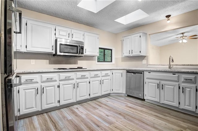 kitchen featuring light hardwood / wood-style floors, white cabinets, a skylight, appliances with stainless steel finishes, and ceiling fan