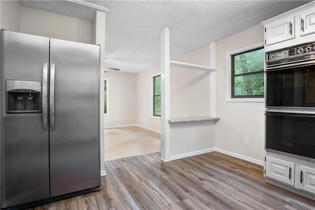 kitchen featuring a textured ceiling, light hardwood / wood-style flooring, white cabinetry, double oven, and stainless steel refrigerator with ice dispenser