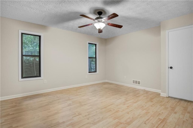 spare room featuring a textured ceiling, a healthy amount of sunlight, light hardwood / wood-style floors, and ceiling fan