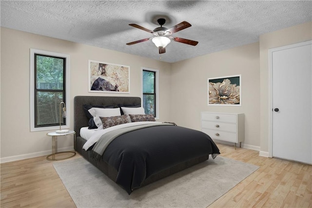 bedroom with multiple windows, a textured ceiling, ceiling fan, and light hardwood / wood-style flooring