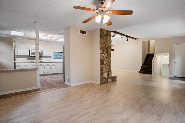 unfurnished living room featuring light hardwood / wood-style floors, ceiling fan, track lighting, and a textured ceiling