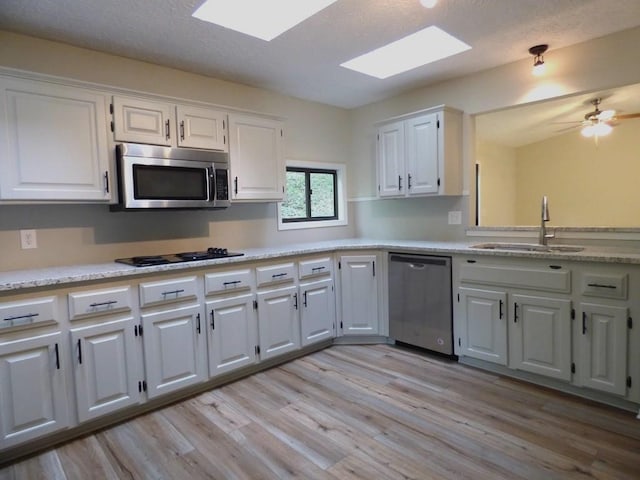 kitchen featuring white cabinetry, stainless steel appliances, light hardwood / wood-style flooring, a skylight, and sink