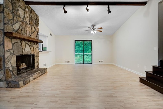 living room featuring a stone fireplace, ceiling fan, beamed ceiling, and light hardwood / wood-style flooring