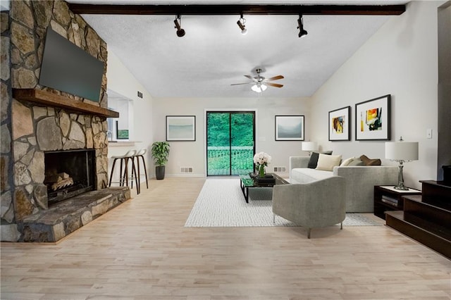 living room featuring ceiling fan, vaulted ceiling with beams, a fireplace, and light hardwood / wood-style floors