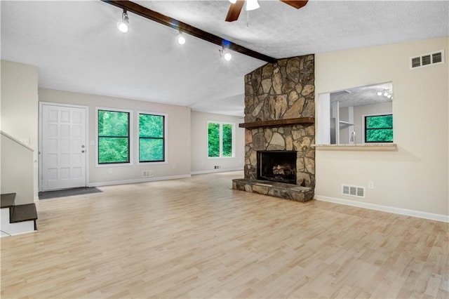 unfurnished living room featuring a fireplace, light wood-type flooring, a textured ceiling, ceiling fan, and vaulted ceiling with beams