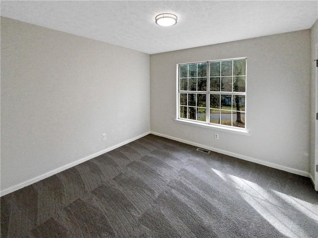 spare room featuring dark colored carpet, visible vents, baseboards, and a textured ceiling