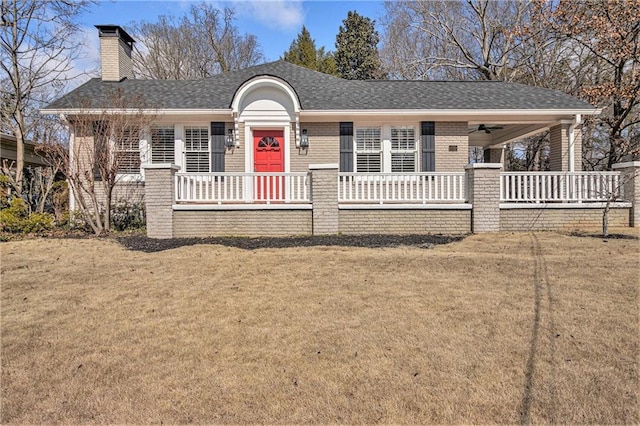 view of front facade with covered porch, a chimney, brick siding, and a front yard