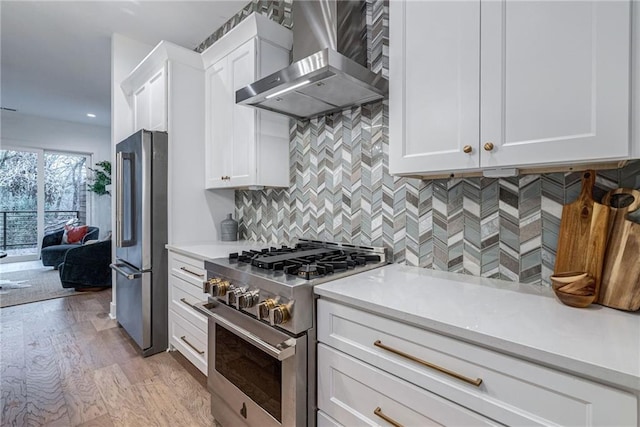 kitchen with premium appliances, light hardwood / wood-style floors, white cabinets, and wall chimney exhaust hood