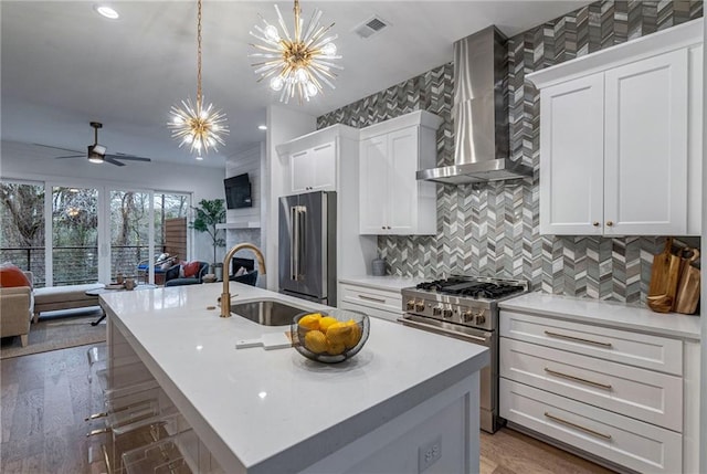 kitchen with high end appliances, sink, wall chimney range hood, and an island with sink