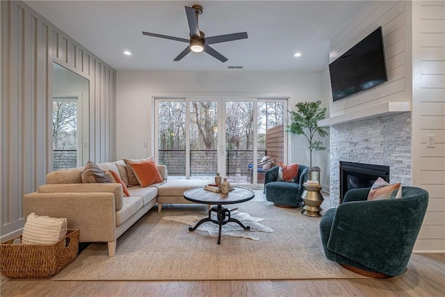 living room with a stone fireplace, light hardwood / wood-style floors, and ceiling fan