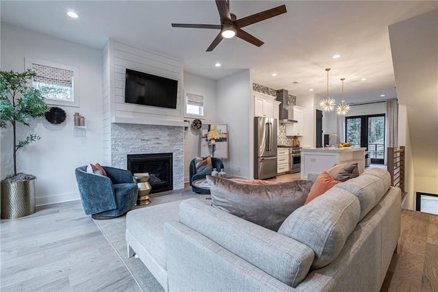 living room with sink, ceiling fan with notable chandelier, a fireplace, and light wood-type flooring