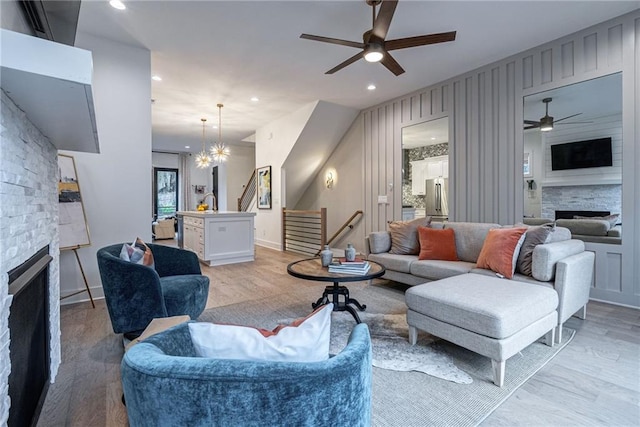 living room featuring a stone fireplace, light hardwood / wood-style flooring, and ceiling fan with notable chandelier