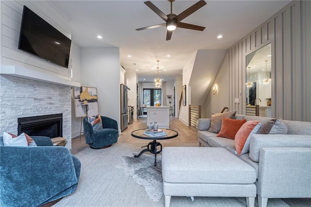 living room with a stone fireplace and ceiling fan with notable chandelier