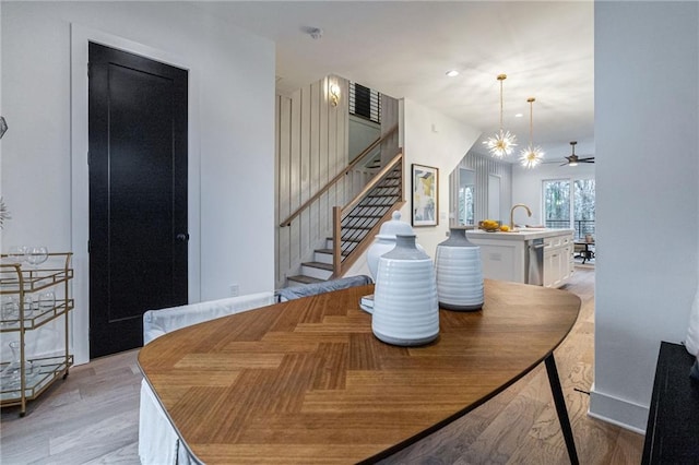 dining space with sink, ceiling fan with notable chandelier, and light hardwood / wood-style floors