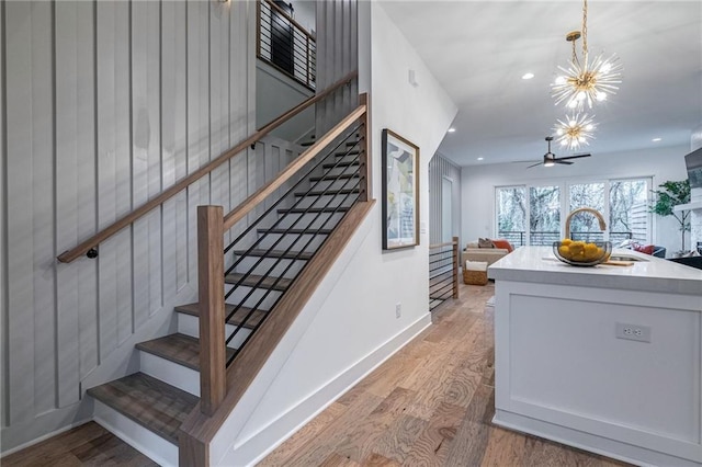 staircase featuring wood-type flooring and ceiling fan with notable chandelier