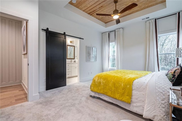 bedroom with wood ceiling, ensuite bath, a raised ceiling, ceiling fan, and a barn door