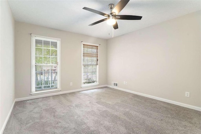 carpeted spare room featuring ceiling fan, visible vents, and baseboards