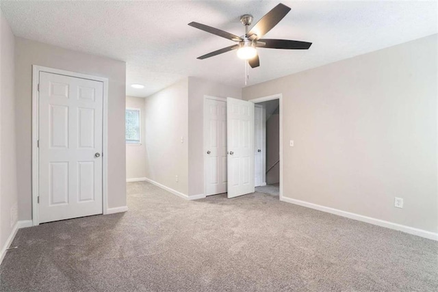 unfurnished bedroom with a textured ceiling, ceiling fan, baseboards, a closet, and carpet