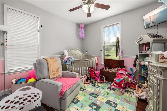 bedroom with wood-type flooring, a nursery area, and ceiling fan