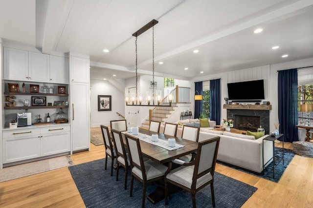 dining space with a fireplace, light hardwood / wood-style floors, an inviting chandelier, and beamed ceiling