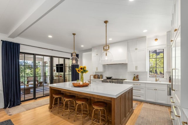 kitchen with pendant lighting, light wood-type flooring, a center island with sink, and white cabinetry